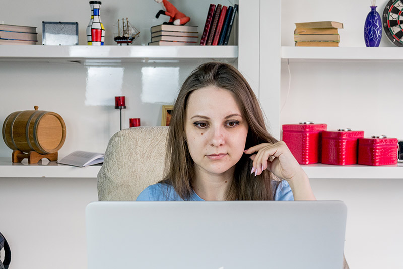 woman sitting at a desk in a contemplating manner as she looks at the screen on her laptop
