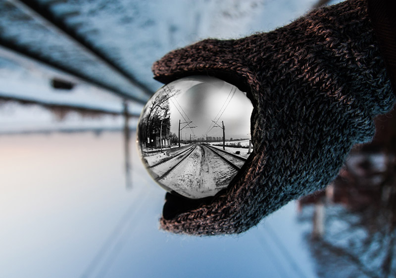 Looking through a sphere, train tracks in the snow leading away from the camera