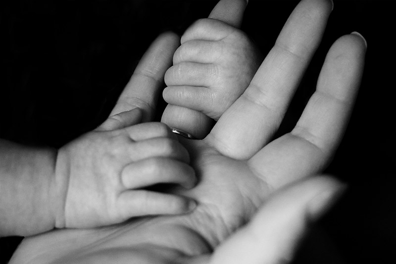 Newborn baby's hands grasping an adult's hand