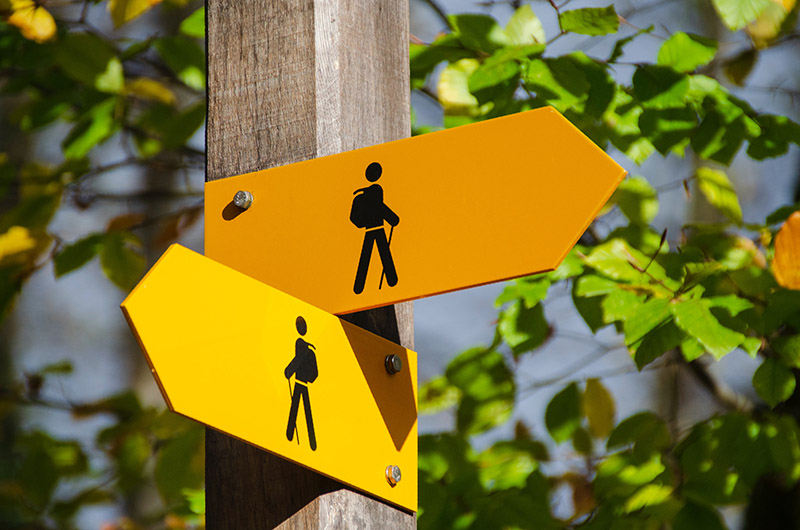 Two yellow sign posts, each facing the other direction.  Each sign has a stick figure of hiker walking
